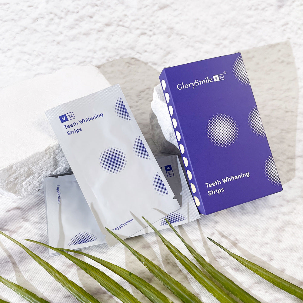 GlorySmile teeth whitening strips packaging on a textured white surface with green leaves.
