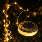A hanging solar-powered string light with a warm white glowing globe and a dark solar panel top, shown against a black background.