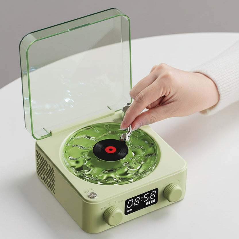Green Vinyl Wireless Bluetooth Speaker with a hand placing a record on it, on a white surface.