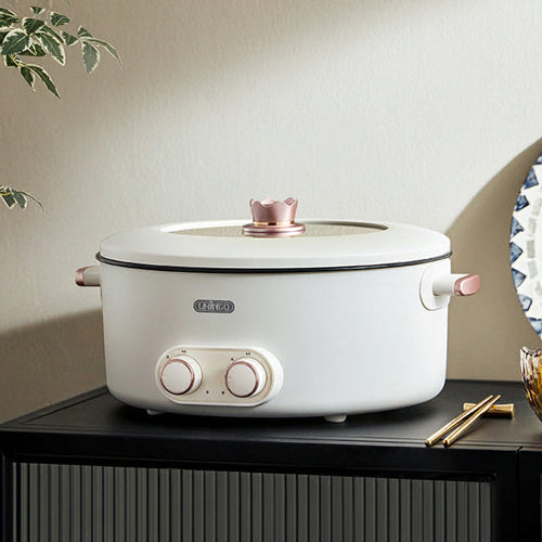 White electric pot with pink accents on a black cabinet against a beige wall.