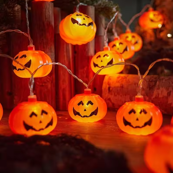 String lights shaped like jack-o'-lanterns on a wooden surface with Halloween decorations.