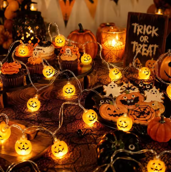 Warm white Halloween LED Pumpkin Lantern Decorative Lights, glowing on a decorated Halloween table with cupcakes, cookies, pumpkins, spiderwebs, and a 'Trick or Treat' sign.